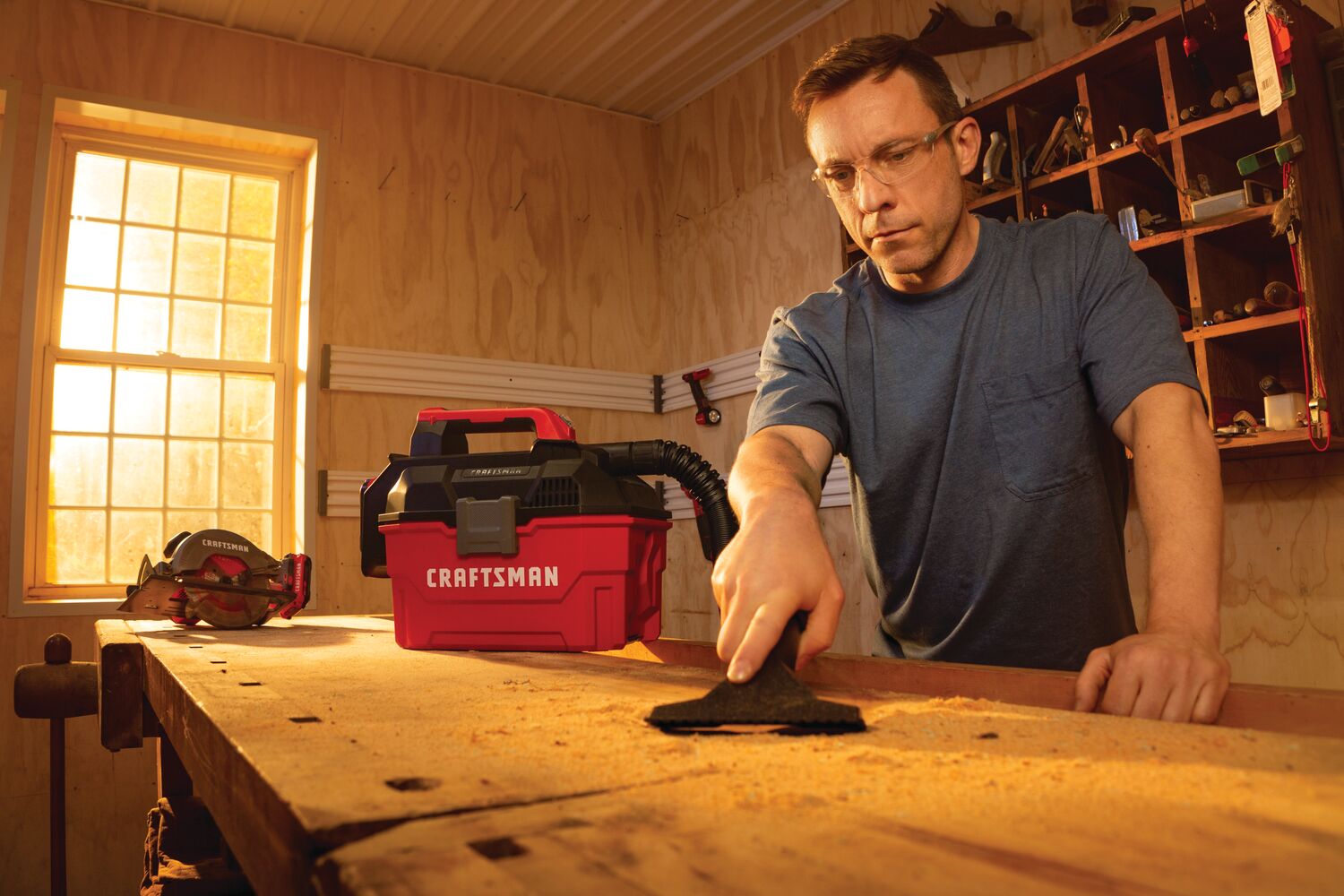 20 volt cordless 2 gallon wet dry vacuum being used by a person to clean wooden work station.