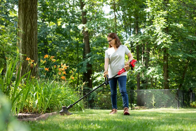 CRAFTSMAN V20 BRUSHLES PR String Trimmer trimming around flowerbed with trees in background